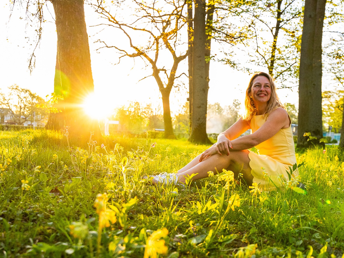 Yvonne Schneider sitzt lachend auf einer Frühlingswiese in der Abendsonne